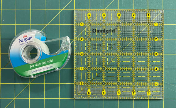 A square ruler with Nexcare tape applied to the top and bottom edges